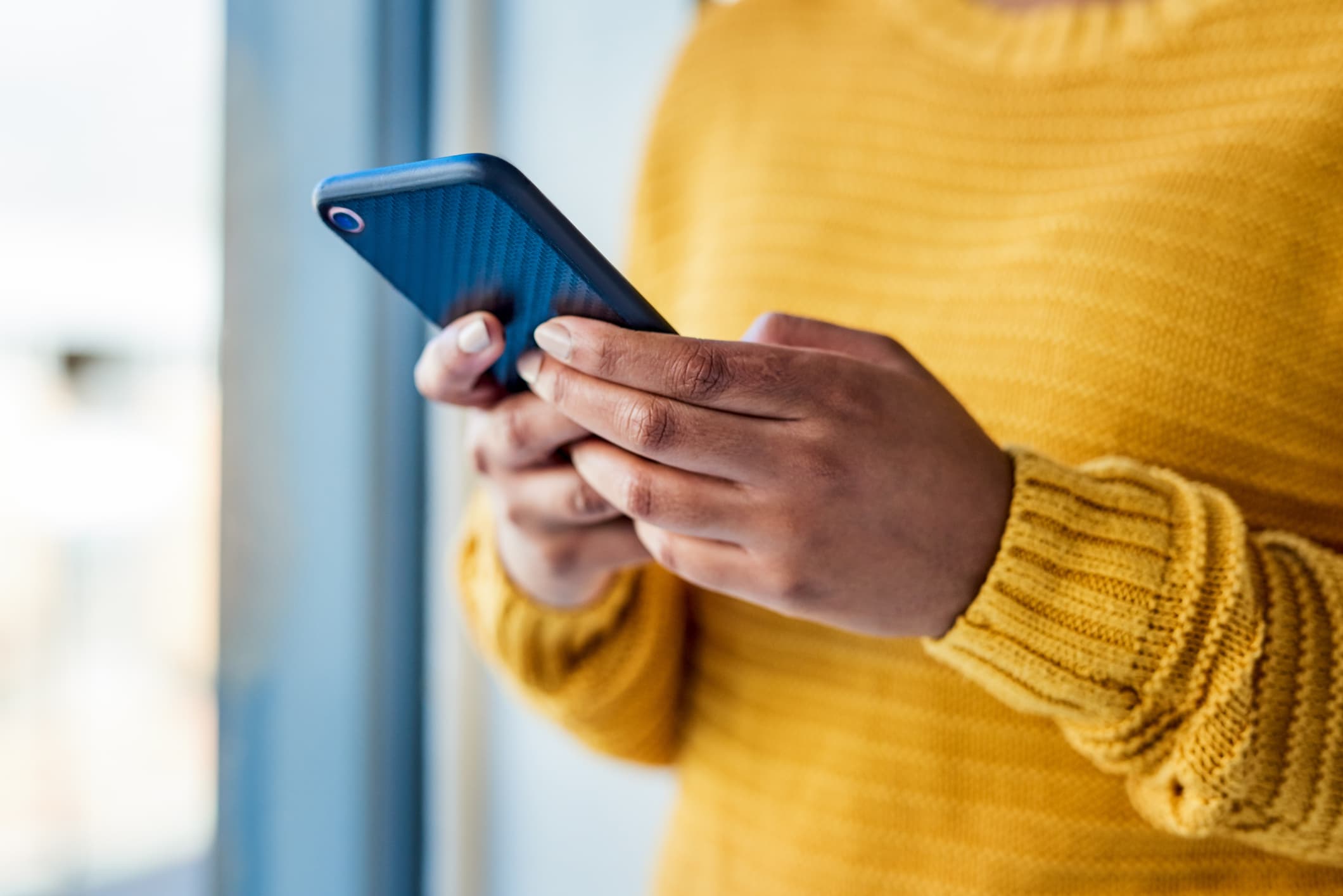Person in a yellow sweater typing on a smartphone